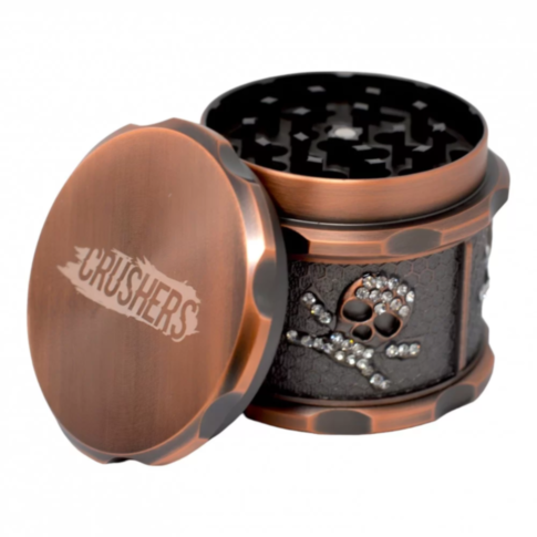 The 63mm 4pc Crushers Skull Printed Grinder is a stylish bronze herb grinder adorned with a skull and crossbones design embellished with rhinestones. The lid features the word CRUSHERS, and upon opening, sharp teeth are revealed inside, making it ideal fo