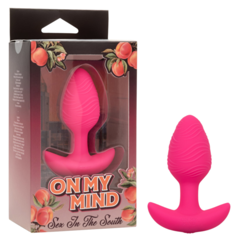 The image shows a pink silicone plug with a textured surface next to its packaging, which features peach illustrations and the product name On My Mind–Sex in the South, suggesting intense vibration for elevated pleasure.