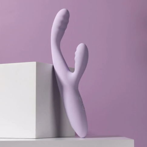 The Svakom-CiCi 2+ Heating Rabbit-Lilac, a beginner-friendly vibrator designed for luxurious G-spot stimulation, leans elegantly against a white cube. It showcases a curved design with textured grips and buttons, all set against a soft lilac background fo