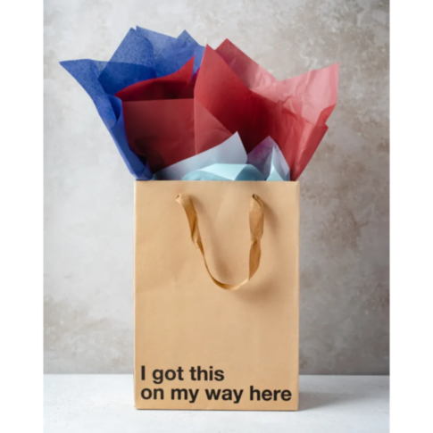 A snarky Wood Rocket-I Got This On My Way Here Bag with twisted handles, filled with red, blue, and light blue tissue paper, is set against a light textured background. Emblazoned with the phrase "I got this on my way here," it perfectly embodies the quin