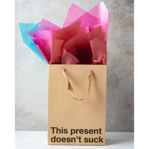 The Wood Rocket-Doesn't Suck Bag, featuring a neutral stone texture background and rope handles, is filled with pink and blue tissue paper. It’s ideal for a snarky gift at a white elephant party, boasting the playful text 