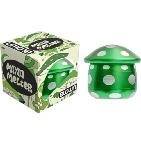 Green mushroom-shaped spinning top with white dots, positioned beside its box labeled 4pc Blown Aluminum Mushroom Grinder. The box features a green leaf pattern and a matching mushroom design, reflecting the sleek style of the Blown Aluminum Mushroom Grin