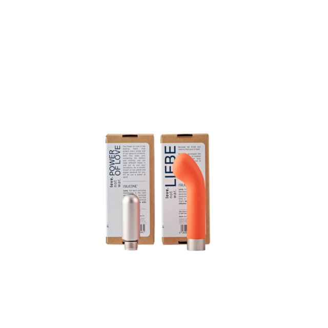 Two vibrators are showcased, with one being a sleek silver cylinder and the other an orange curved design specifically for G-spot stimulation. Both stand upright in front of two brown cardboard boxes labeled Libre and Power of Love. Made from NeoSilicone,