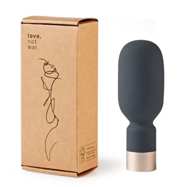 A sleek, grey, cylindrical object named the Love Not War-Koi Mini Wand with a rounded top and gold base stands next to a cardboard box that features an abstract line drawing along with the text "Love Not War." The box emphasizes its NeoSilicone material a
