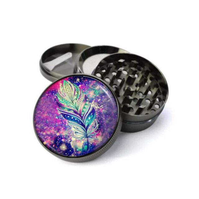 The 4pc Grinder Galaxy Feather is a zinc-plated steel grinder with CNC razor-sharp teeth, three compartments, and a magnetic grinding area. Its lid features a vibrant multicolored feather design on a colorful cosmic background.