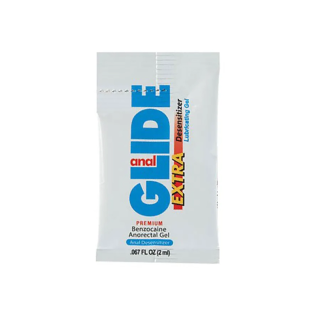 A single-use Anal Glide Extra desensitizer pillow pack, a premium benzocaine and water-based gel lubricant, is shown upright with blue, red, and yellow text on a white background. Each packet contains 2 mL (0.067 fl oz) of product.