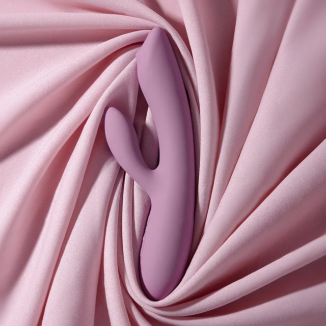A Svakom-Trysta Neo G Spot Rolling Ball Rabbit-Rose in pink silicone sits elegantly on soft, draped pink fabric, creating a smooth aesthetic.
