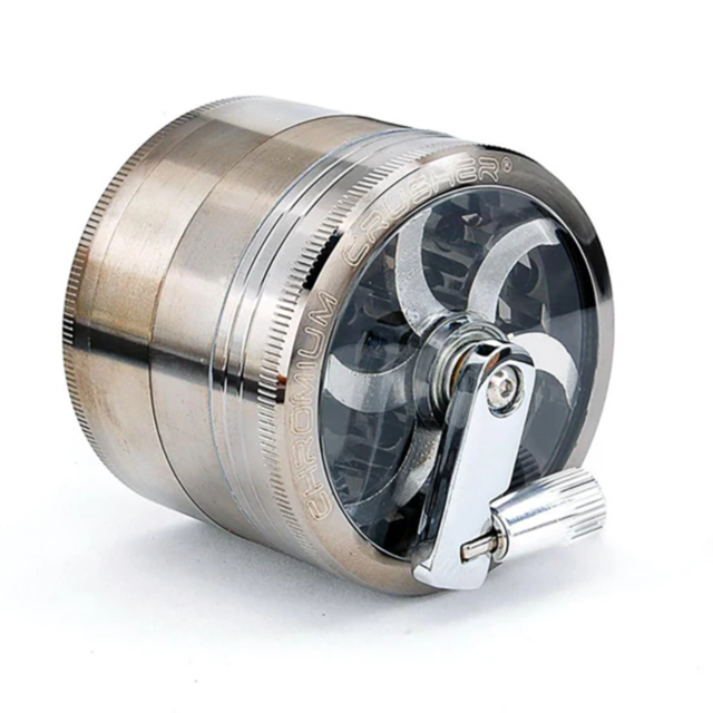 The 63mm 4pc Crushers Crank Top Metal Grinder is a metallic herb grinder that has diamond-shaped teeth and a circular, transparent top showing the grinding blades inside. It is labeled with CHROMIUM CRUSHER on the side and includes a convenient side handl