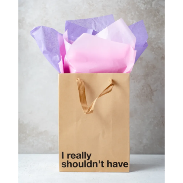 Introducing the "Wood Rocket-I Really Shouldn't Have Bag," this gift bag features a snarky phrase and comes in an elegant brown color with brown handles. It is filled with pink and purple tissue paper, set against a textured, light-colored surface, making