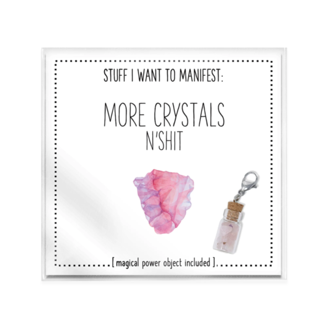 The More Crystals n Shit Card w Charm features a framed print that reads, “STUFF I WANT TO MANIFEST: MORE CRYSTALS NSHIT,” along with a magical power object. It displays illustrations of a pink crystal cluster and a small corked bottle with a clip, captur