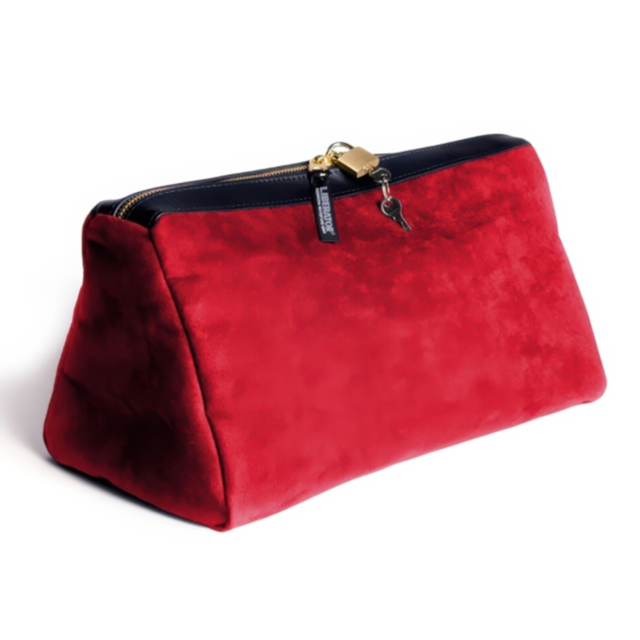 The Tallulah Locking Toy Case in Cinnabar microsuede features a vibrant red hue with a gold zipper and small lock, adding sophistication to your bedroom accessories. Its structured, trapezoidal shape stands upright, with the key attached by a black tag ag