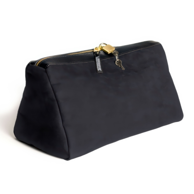 The Tallulah Locking Toy Case Microsuede-Black is a black designer handbag equipped with a gold zipper and keyed lock. Its structured, trapezoidal shape and smooth microsuede texture give it a sleek and elegant look.