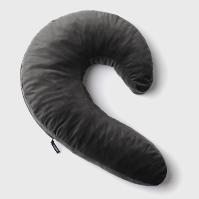 The Lune Side Snuggler Pillow-Black, a crescent-shaped cushion in dark gray, is presented on a simple white backdrop. Perfect for side sleepers, it offers plush softness with shredded memory foam and includes a small tag on one side.