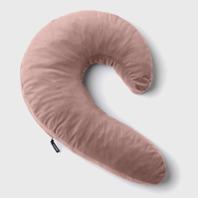 The Lune Side Snuggler Pillow-Rose, ideal for side sleepers, is a pink, crescent-shaped pregnancy pillow featuring a white backdrop. Its shredded memory foam filling provides outstanding comfort and support.