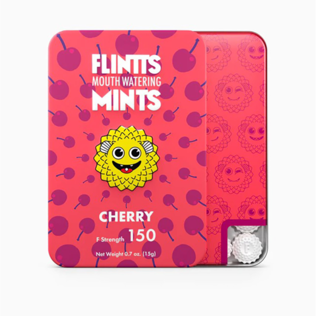 A large group of people is closely gathered on a green field at an outdoor event, smiling and looking at the camera. They are surrounded by trees and a crowd, enjoying Flintt Mints Cherry F Strength 150 amidst a lively atmosphere under the clear, sunny sk