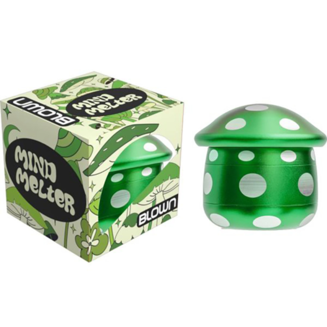 Green mushroom-shaped spinning top with white dots, positioned beside its box labeled 4pc Blown Aluminum Mushroom Grinder. The box features a green leaf pattern and a matching mushroom design, reflecting the sleek style of the Blown Aluminum Mushroom Grin