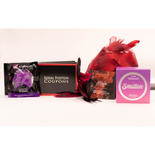 The Loveable Getaway Kit by Starship includes a vibrant selection of adult novelty items like a sexual position coupon booklet, vibrating ring, warming intimate glide for romantic getaways, and a massage candle, all playfully set with red feathers on a wh