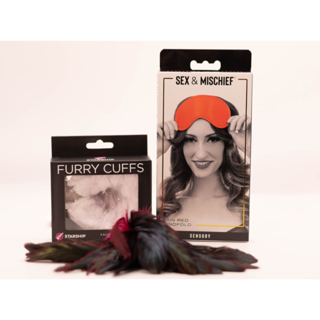 The Curated Kit by Starship – Sexy Kit displays boxes of red blindfolds with a smiling person, alongside furry handcuffs. Feathers are scattered in front, adding texture.